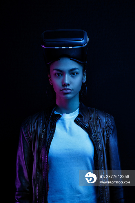 African-American girl in vr glasses with a virtual reality headset isolated on a black background, illuminated by neon lights