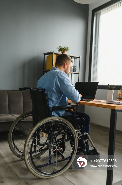 Young happy entrepreneur in wheelchair working on laptop at home.