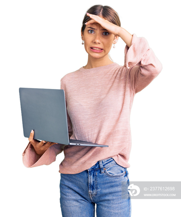 Beautiful caucasian woman with blonde hair working using computer laptop stressed and frustrated with hand on head, surprised and angry face