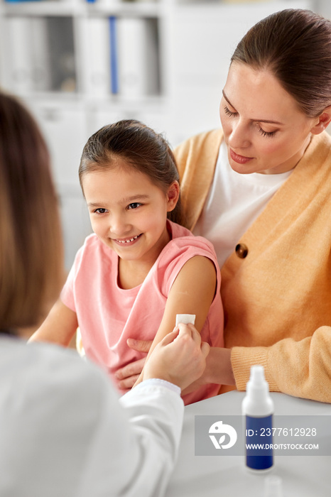 medicine, healthcare and pediatry concept - female doctor or pediatrician disinfecting arm skin of little girl patient with mother at clinic