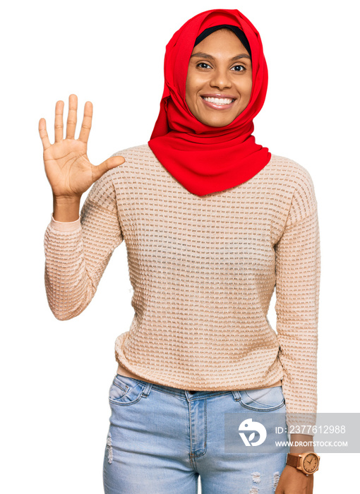 Young african american woman wearing traditional islamic hijab scarf showing and pointing up with fingers number five while smiling confident and happy.