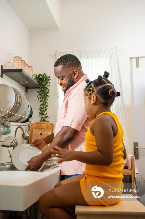 African father teaching little daughter washing dishes in the sink on kitchen counter with talking together after having dinner. Happy family dad and child girl kid spending time together at home.