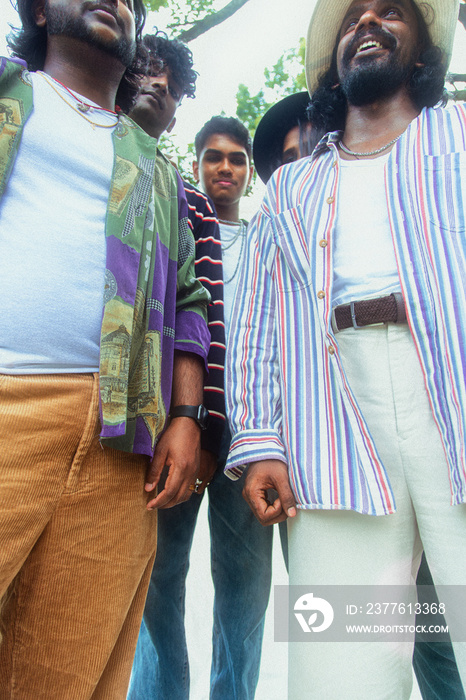 Malaysian Indian men posing and laughing together in a group setting, outdoors, in a park against a cloth backdrop