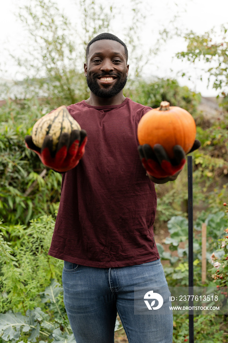 Portrait of smiling man holding pumpkins in urban garden