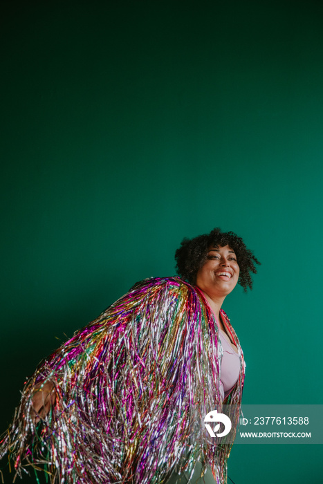 person in a rainbow tinsel jacket smiling and dancing