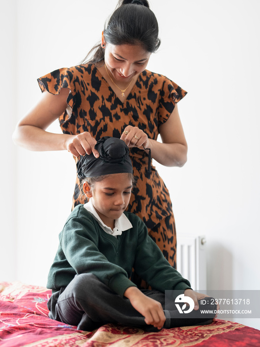 Mother wrapping traditional turban on son’s (6-7) head