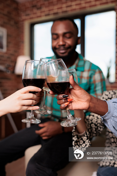 Joyful multiracial group of best friends toasting wineglasses while enjoying wine party at home. Happy smiling diverse people clinking glasses while celebrating birthday event.