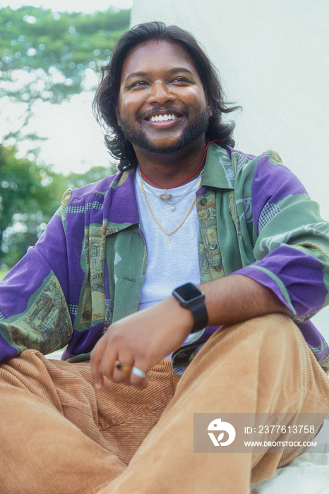 Malaysian Indian men in a group against a cloth backdrop in a park surrounded by trees, talking, laughing and sitting together