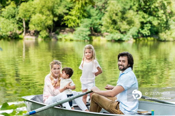 Happy young family riding boat on lake at park and looking at camera