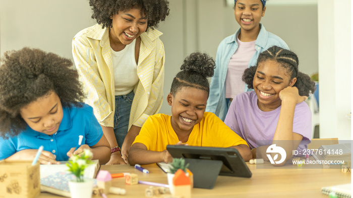 A group of young African kids with their sister use a tablet to communicate with friends. Happy kids use computer for online class under support from a young female teacher. Technology for education