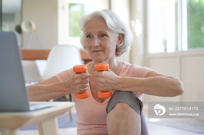 Senior woman doing fitness exercises with virtual class, holding dumbbells