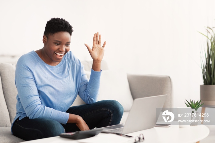 Black woman having videocall using laptop waving hand