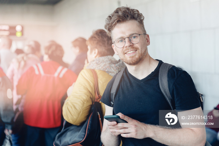 Portrait happy Traveler young curly man with backpack stands in line to board plane use smartphone