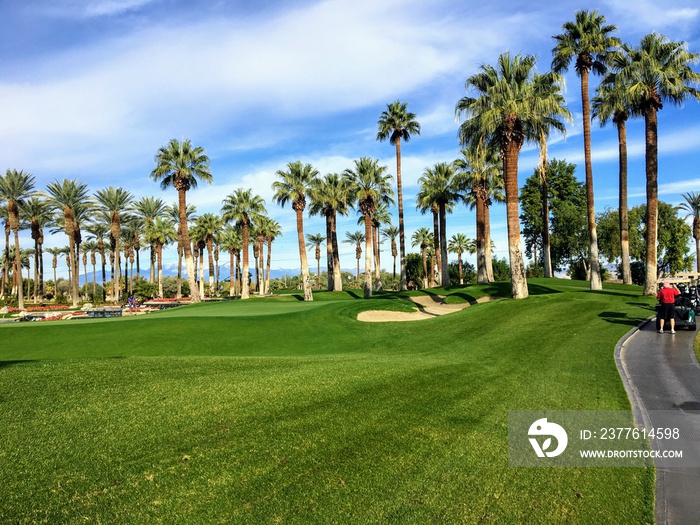 A young male golfer walking towards the green on a par 4 surrounded by water on a golf course in the desert oasis of Palm Springs, California, United States of America.