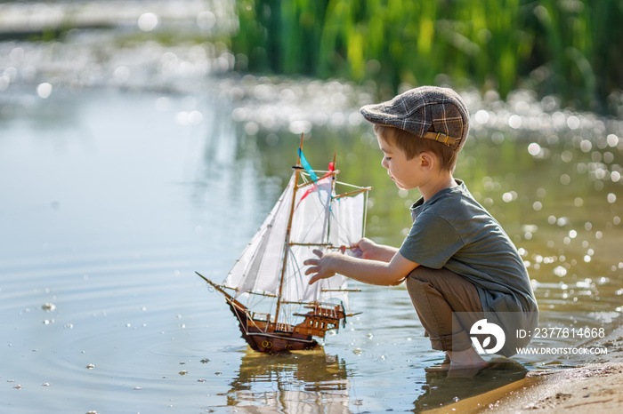 little boy in cap launching ship on the river