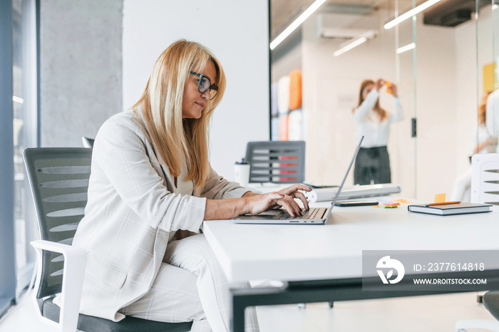 Woman in formal clothes sitting in the office and working by using laptop