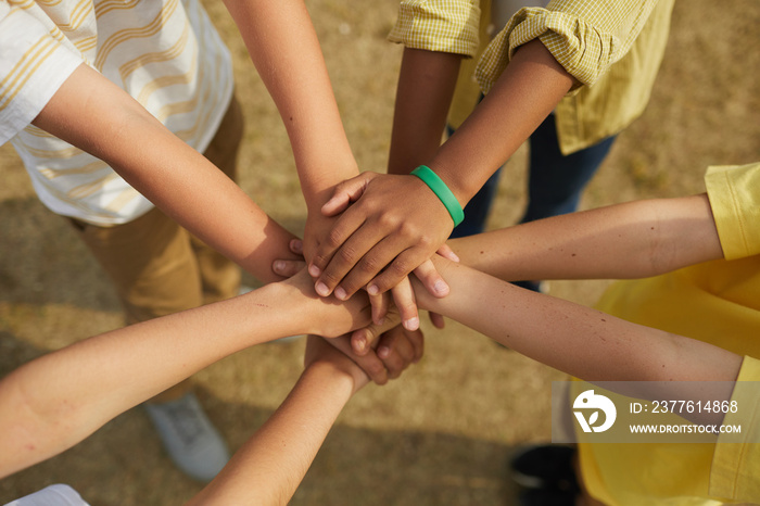 Top view close up at multi-ethnic group of children stacking hands while standing in circle outdoors, concept of friendship and unity