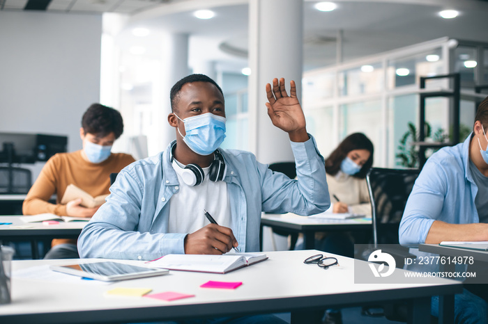 Black guy student raising hand, wearing medical mask