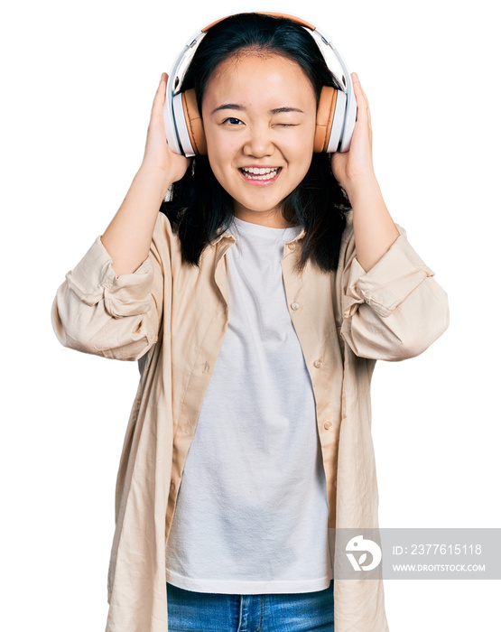 Young chinese woman listening to music using headphones winking looking at the camera with sexy expression, cheerful and happy face.