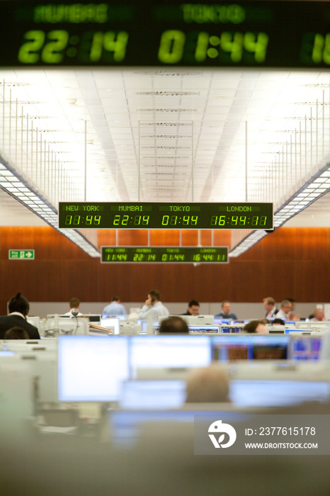 Digital time zone clock hanging over business colleagues working on trading floor