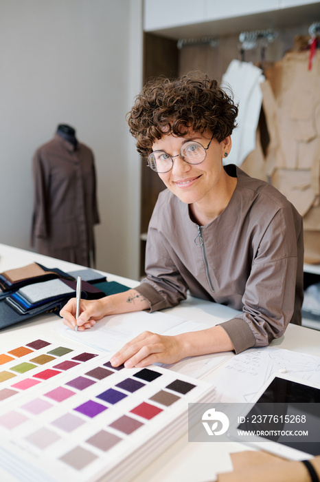 Young designer making notes and looking through catalogue of textile samples