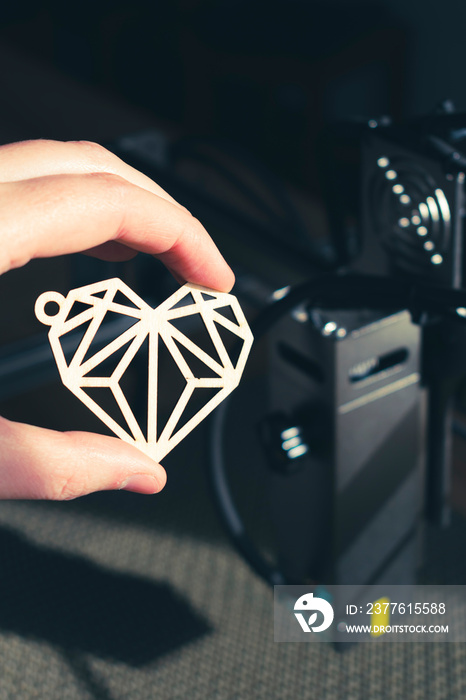 Laser engraving and cutting, hand holding an example of a cut out wooden heart