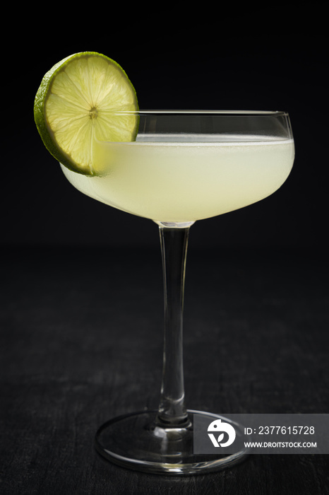 Elegant and bright Daiquiri cocktail with a lime wheel on a black table