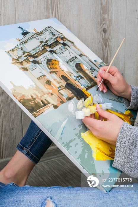 Female hands coloring canvas Picture by numbers girl Triumphal Arch Paris. Creative hobby. Painting for beginners. Leisure activity for stay home isolation, anti-stress idea. Meditation, relax concept
