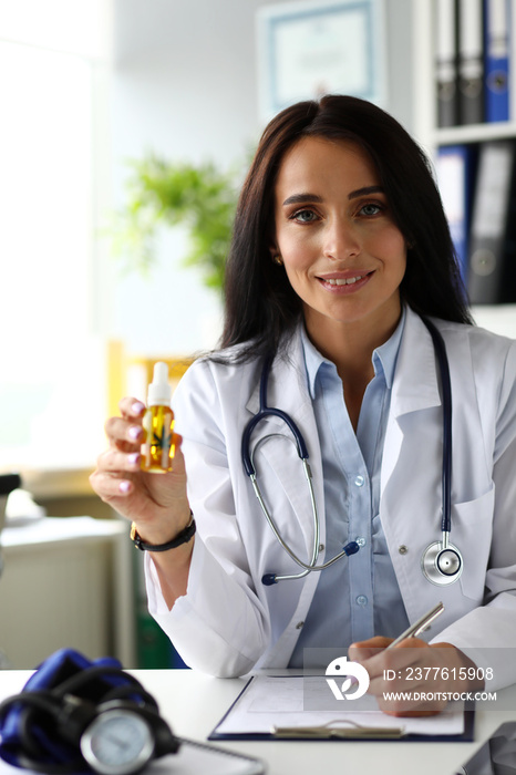 Pretty cheerful female GP giving to patient dropper jar of cannabis concentrate oil during consultation close-up