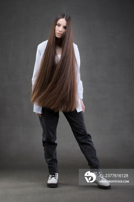 A beautiful girl with very long hair in full growth on a gray background.