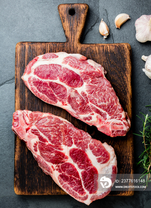 Raw pork cutlet chop for grill BBQ with herbs on wooden board, slate background, top view, copy spaces