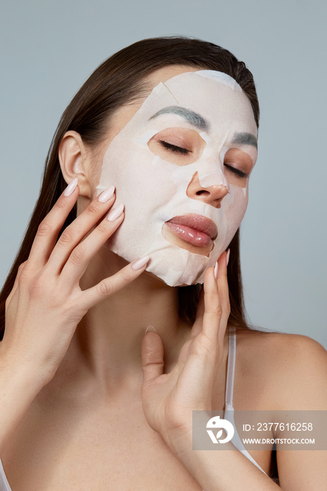 Beauty face skin care. Woman apply a cloth moisturizing mask on face . Girl model with cosmetic mask. Facial  treatment