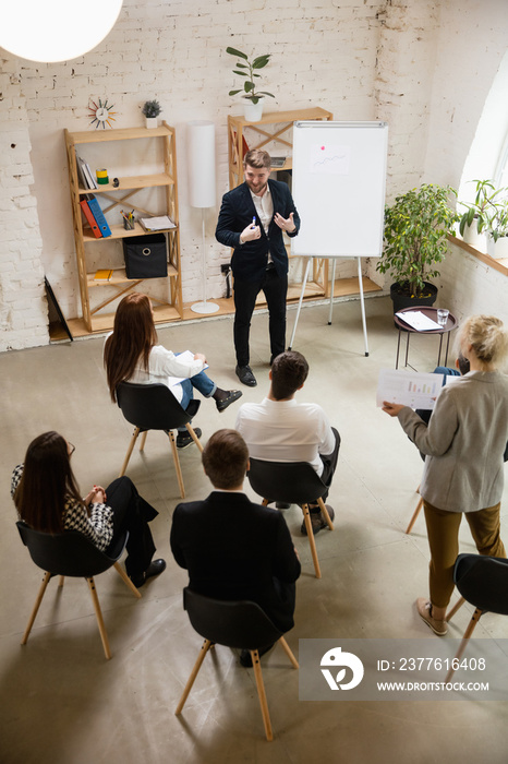 Male speaker giving presentation in hall at university workshop. Audience or conference hall. High angle view of unrecognized participants. Scientific, business conference event, training. Education