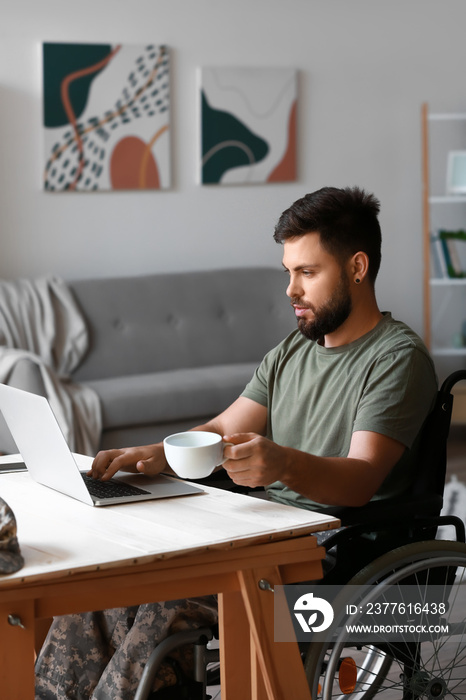 Soldier in wheelchair with cup of coffee using laptop at home