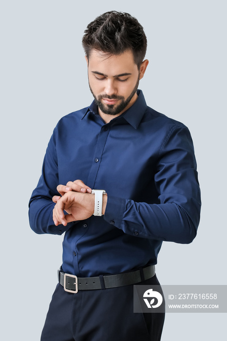 Handsome businessman looking at smart watch on light background