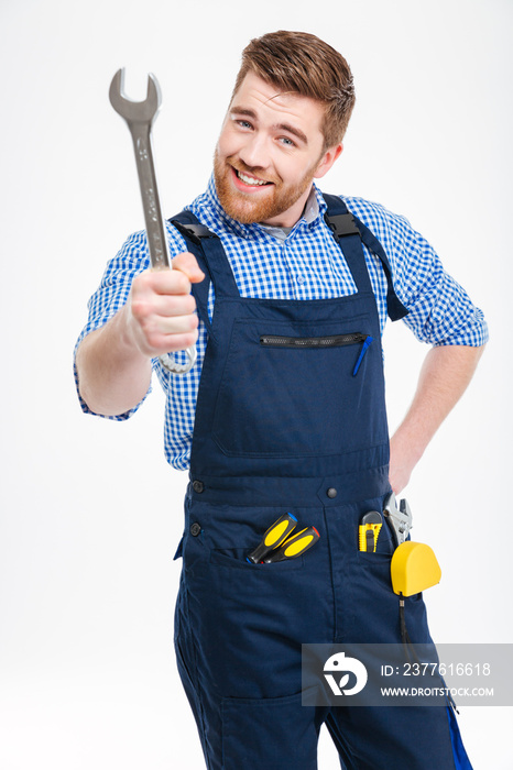 Smiling bearded young man standing and showing wrench