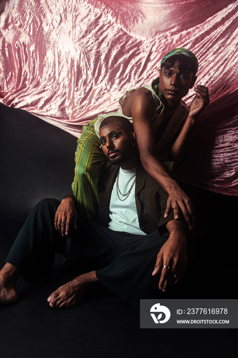 Two Malaysian Indian men in a studio setting with cloth flying in the background, posing against a black bacground