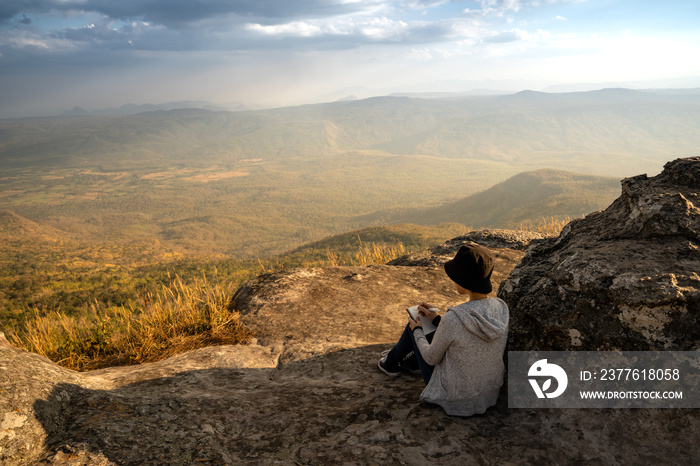 A woman sitting reading and writing looking out at beautiful natural view