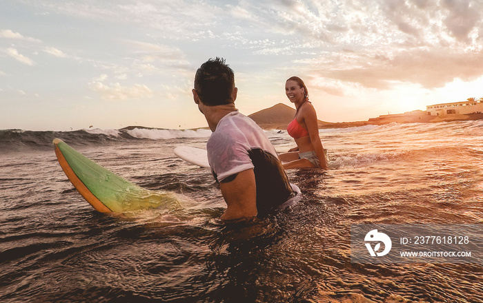 Fit couple surfing at sunset - Surfers friends having fun inside ocean - Extreme sport, travel, adventure, lifestyle and vacation concept - Focus on man head - Original sun color tones