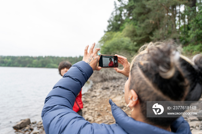 Mother photographing son by lake on hike