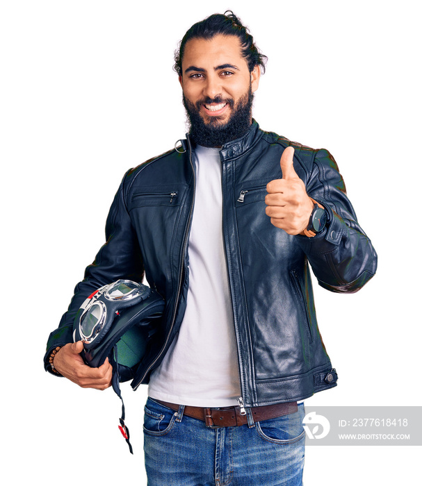 Young arab man holding motorcycle helmet smiling happy and positive, thumb up doing excellent and approval sign