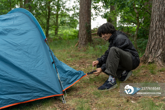 Young man setting up tent in forest