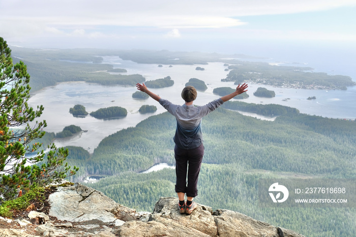 Woman hiker on steep cliff above the ocean with many little islands. Vancouver Island. Tofino. Pacific Rim. British Columbia. Canada