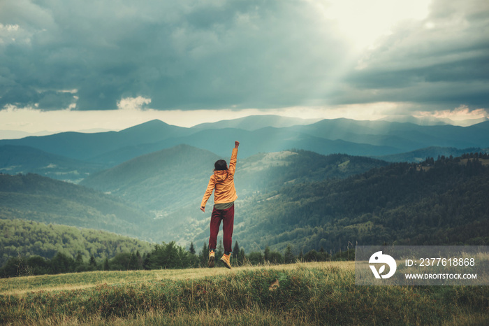 Panoramic view of mountains with an enthusiastic young woman expressing her joy on the hills