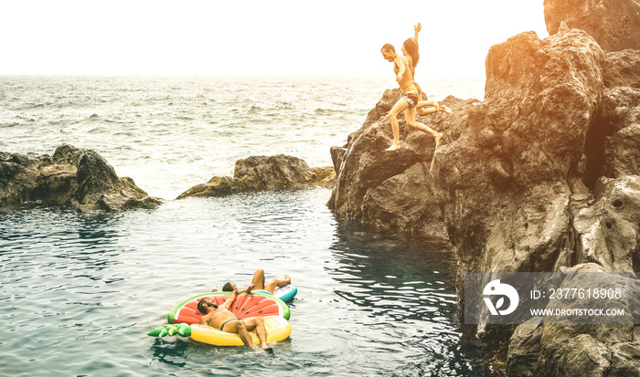 Young friends vacationers jumping on natural pool at travel beach location - Sporty people having fun diving in to the sea - Wanderlust lifestyle concept on warm vintage filter with sunshine halo