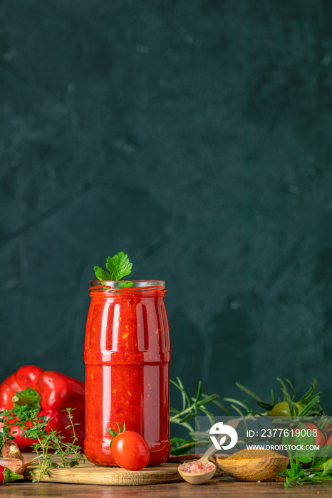 Homemade DIY natural canned hot tomato sauce chutney with chilli or adjika in glass jar standing on wooden table