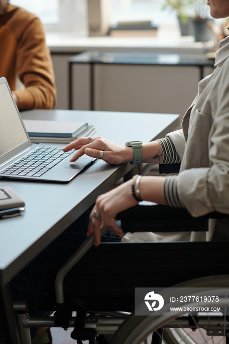 Close-up of young female manager with disability using laptop while sitting in wheelchair by workplace and analyzing online data