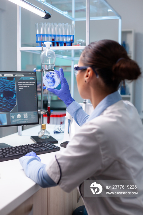 Biologist woman looking at bacteria virus using medical petri dish working at genetic infection experiment in biochemistry hospital laboratory. Scientist doctor examining microorganism sample