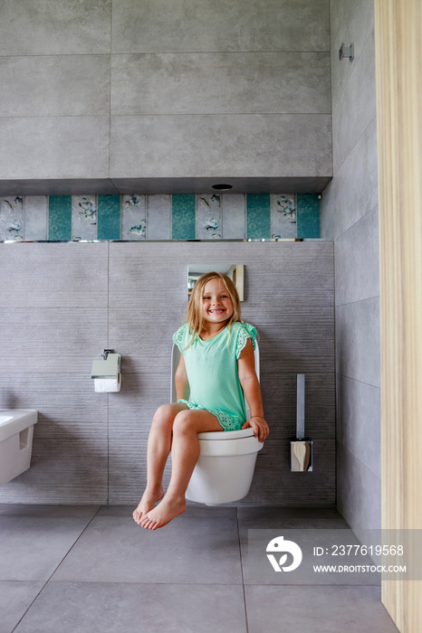 Smiling girl sitting on a toilet in bathroom