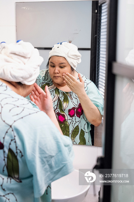 Plus size female examining her skin in the mirror